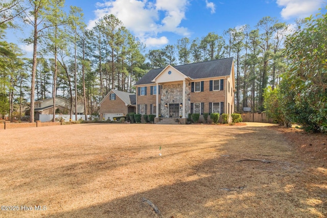 neoclassical / greek revival house with brick siding, stone siding, and a front yard