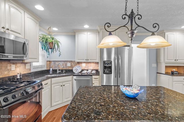 kitchen with sink, appliances with stainless steel finishes, white cabinets, and decorative light fixtures