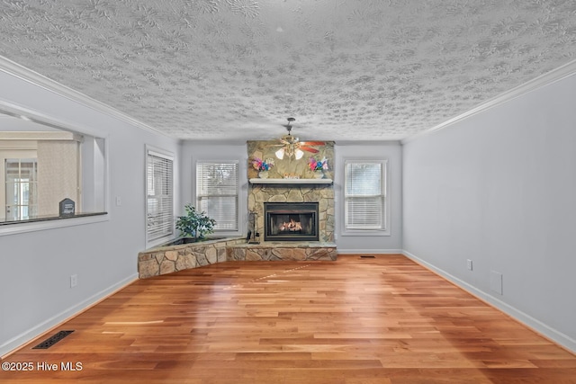 unfurnished living room featuring a healthy amount of sunlight, ornamental molding, light hardwood / wood-style floors, and a stone fireplace