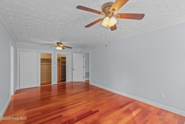 unfurnished bedroom featuring a textured ceiling, ceiling fan, crown molding, multiple closets, and hardwood / wood-style flooring