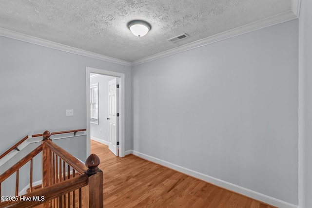 unfurnished room with a textured ceiling, crown molding, and light hardwood / wood-style flooring