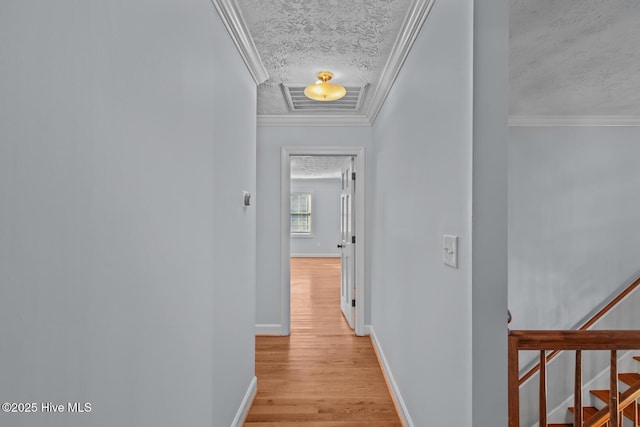 hallway with light wood-type flooring, crown molding, and a textured ceiling