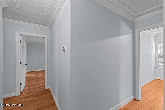 hall with light wood-type flooring, ornamental molding, and a textured ceiling