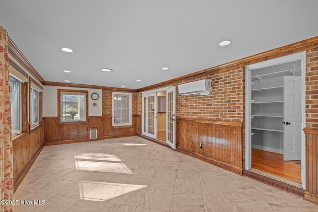 unfurnished room featuring french doors, a wall unit AC, brick wall, ornamental molding, and wooden walls