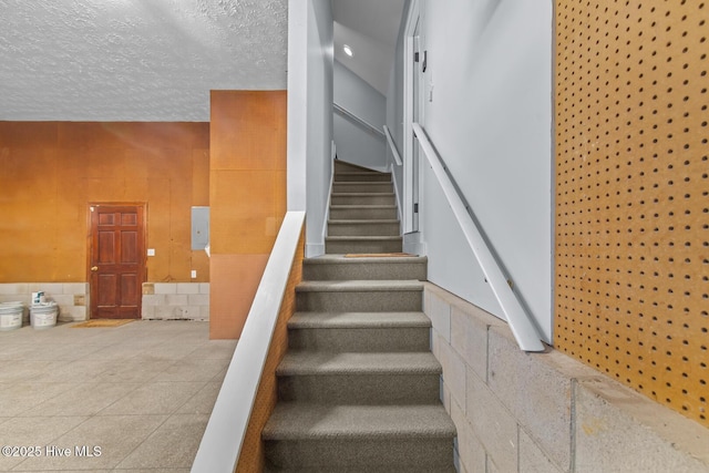 stairway with electric panel and a textured ceiling