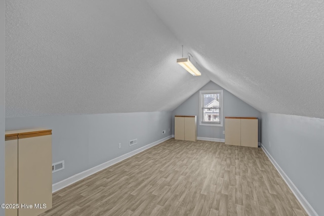 additional living space featuring light wood-type flooring, vaulted ceiling, and a textured ceiling