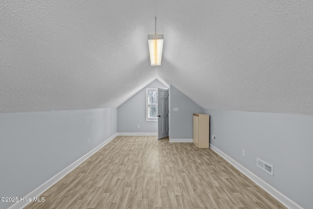 additional living space featuring light hardwood / wood-style floors, a textured ceiling, and lofted ceiling