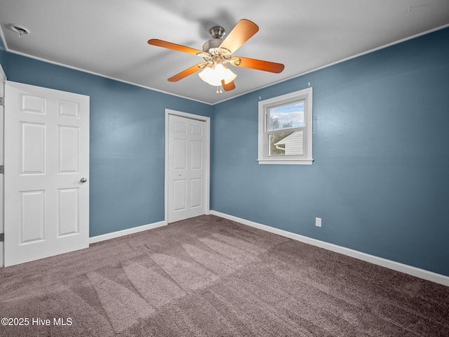 unfurnished bedroom with ornamental molding, baseboards, carpet flooring, a ceiling fan, and a closet