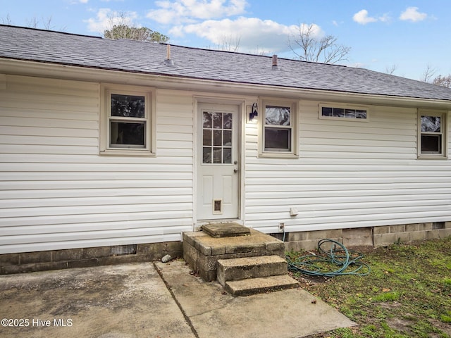 view of exterior entry featuring a shingled roof, a patio, and crawl space