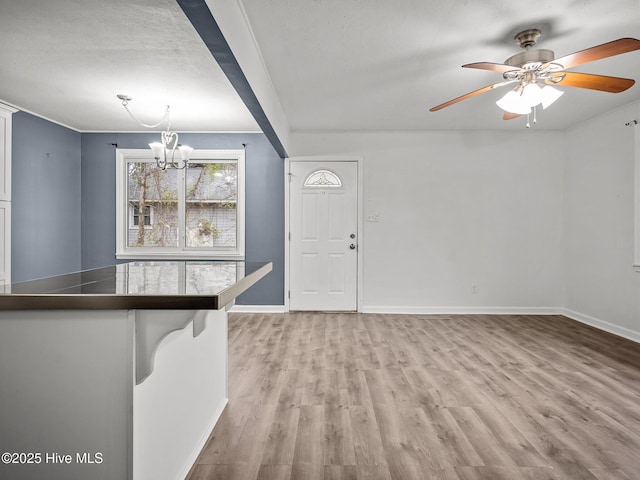 interior space featuring ceiling fan with notable chandelier, baseboards, and light wood finished floors