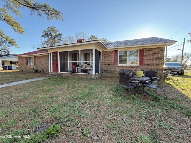 view of front facade with a front yard, a sunroom, brick siding, and metal roof