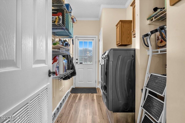 washroom with cabinet space, ornamental molding, a textured ceiling, light wood-type flooring, and independent washer and dryer