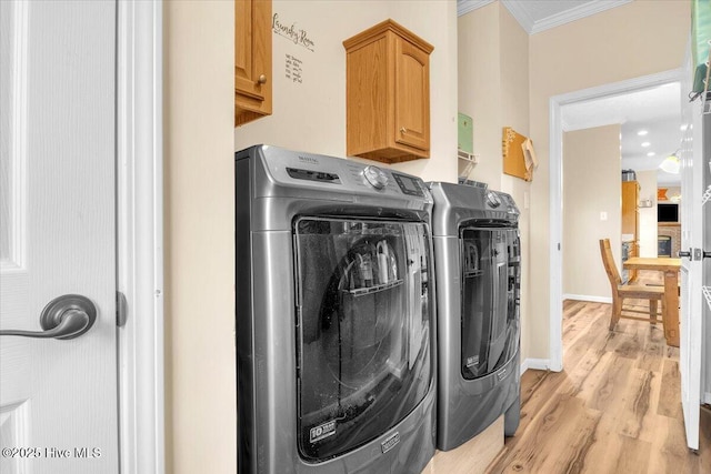 laundry area featuring light wood finished floors, cabinet space, baseboards, crown molding, and washer and dryer