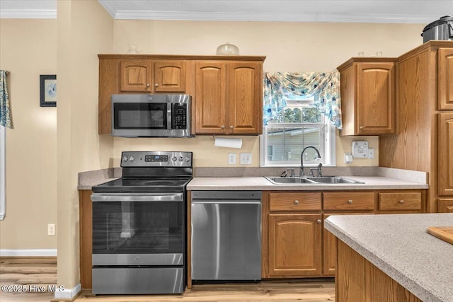 kitchen with appliances with stainless steel finishes, light countertops, a sink, and ornamental molding