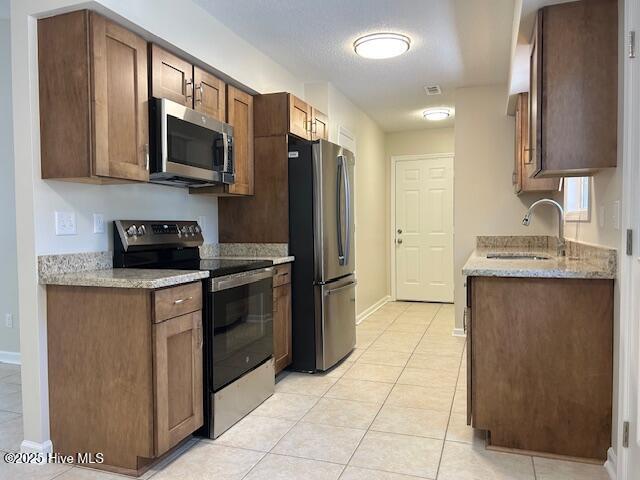 kitchen featuring sink, stainless steel appliances, light stone counters, and light tile patterned floors