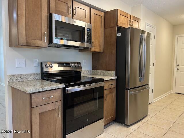 kitchen with appliances with stainless steel finishes, light tile patterned floors, and light stone counters