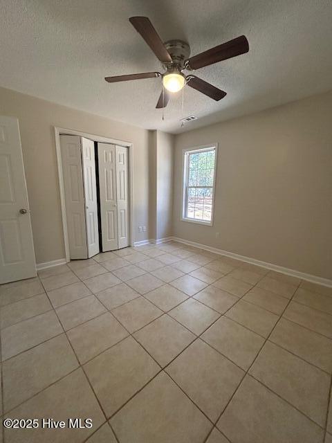 unfurnished bedroom featuring ceiling fan, light tile patterned floors, a textured ceiling, and a closet