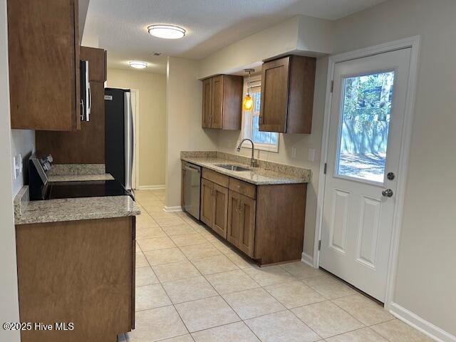 kitchen with light tile patterned floors, sink, stainless steel appliances, and light stone counters