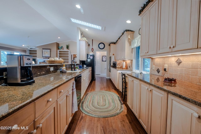 kitchen with tasteful backsplash, lofted ceiling with skylight, stone counters, wood finished floors, and a sink