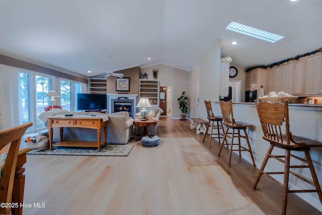 living room featuring a ceiling fan, lofted ceiling, light wood-style floors, and a warm lit fireplace