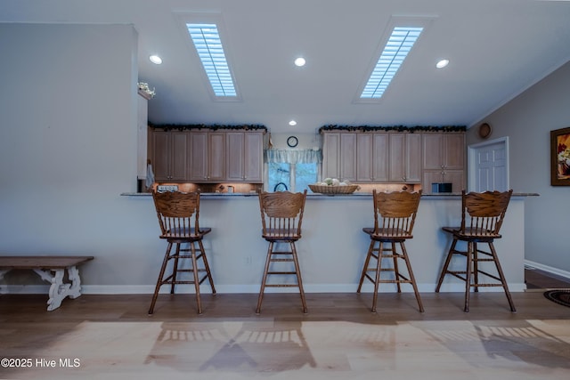 kitchen featuring wood finished floors, a peninsula, a breakfast bar, and a skylight