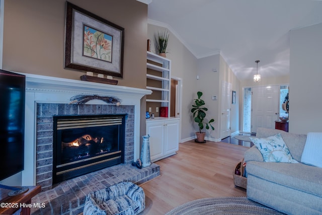 living area featuring a brick fireplace, crown molding, baseboards, vaulted ceiling, and wood finished floors