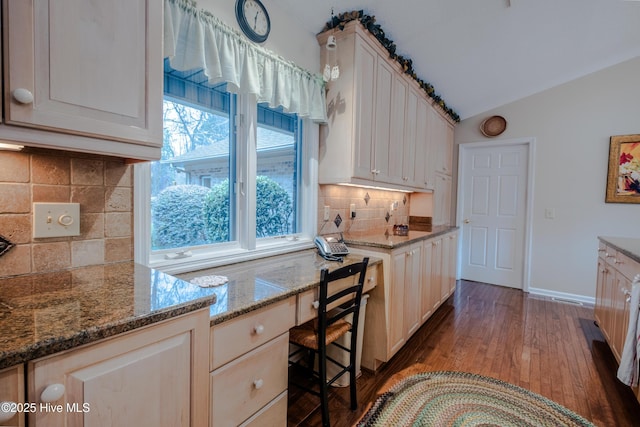 kitchen with backsplash, baseboards, vaulted ceiling, wood finished floors, and stone countertops