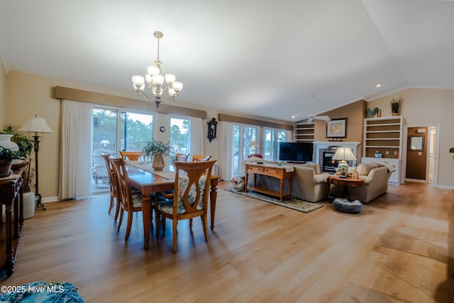 dining space with baseboards, a chandelier, vaulted ceiling, light wood-style floors, and a glass covered fireplace