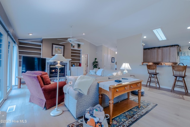 living room featuring a glass covered fireplace, lofted ceiling, visible vents, and light wood-type flooring