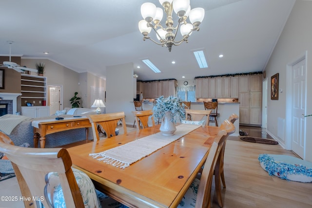 dining room featuring light wood-style flooring, a glass covered fireplace, recessed lighting, baseboards, and vaulted ceiling