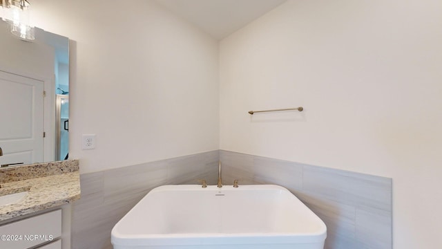 full bath with a wainscoted wall, a freestanding tub, tile walls, and vanity