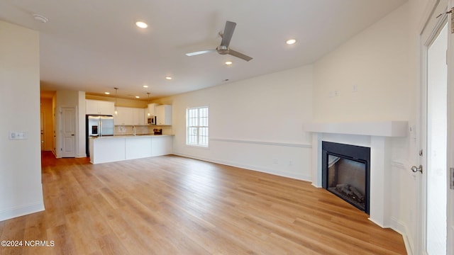 unfurnished living room with a sink, light wood-type flooring, a glass covered fireplace, and recessed lighting