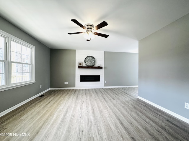 unfurnished living room with visible vents, light wood-style floors, a large fireplace, ceiling fan, and baseboards