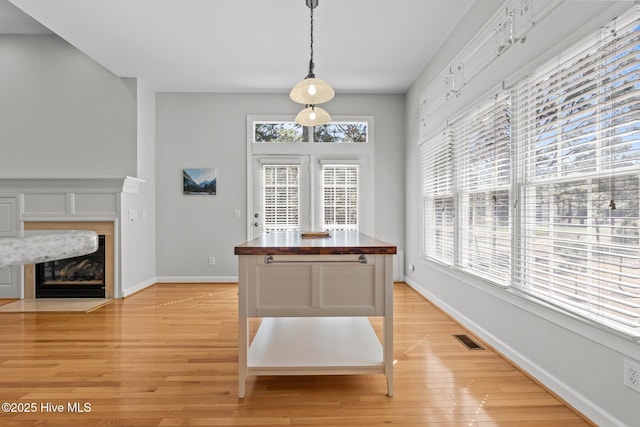 unfurnished dining area with light wood finished floors, visible vents, a fireplace with flush hearth, and baseboards