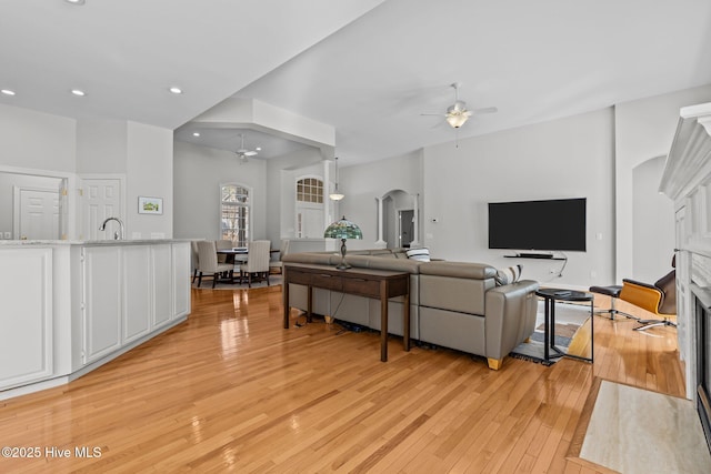 living room featuring light wood finished floors, recessed lighting, a fireplace, arched walkways, and a ceiling fan