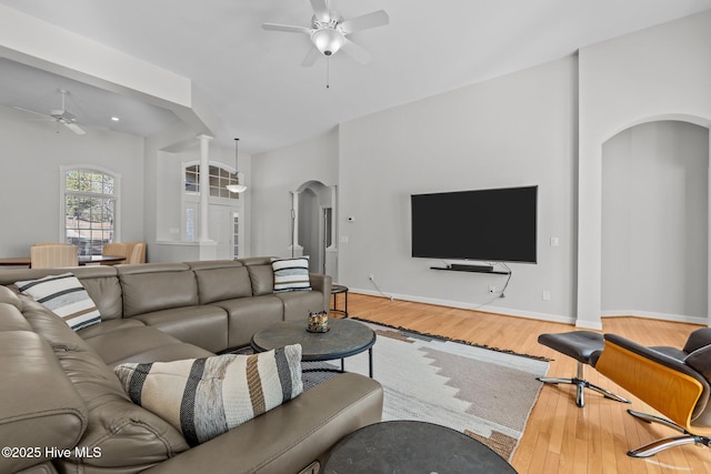 living area with baseboards, arched walkways, wood finished floors, and a ceiling fan