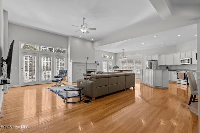 living area with light wood-type flooring, a glass covered fireplace, recessed lighting, baseboards, and ceiling fan