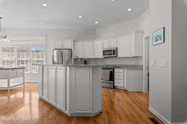 kitchen featuring visible vents, light wood-style flooring, an island with sink, stainless steel appliances, and white cabinetry