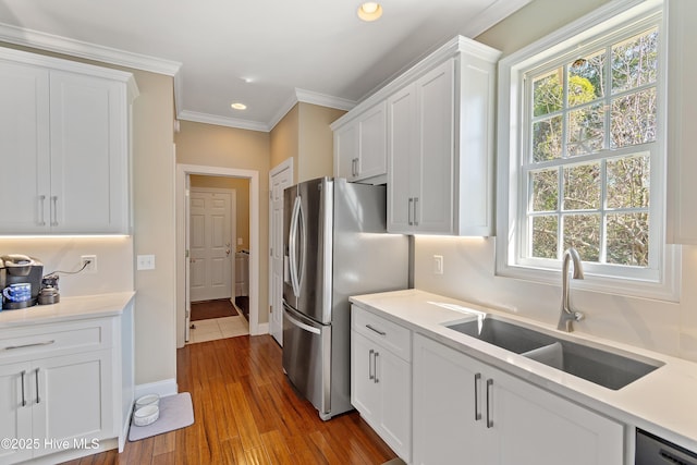 kitchen with wood finished floors, a sink, white cabinetry, ornamental molding, and appliances with stainless steel finishes