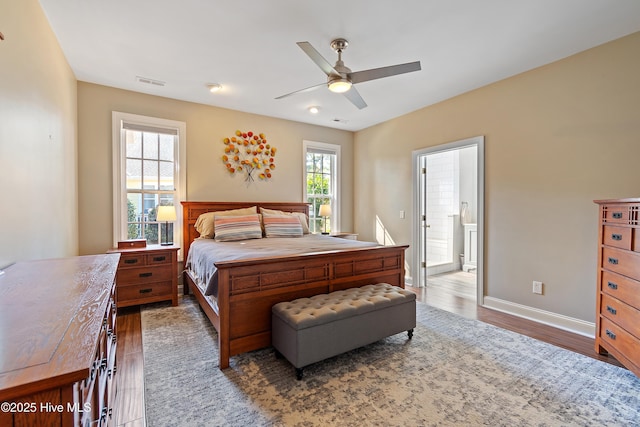 bedroom with ensuite bath, wood finished floors, visible vents, and baseboards