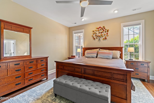 bedroom with baseboards, visible vents, wood finished floors, and multiple windows