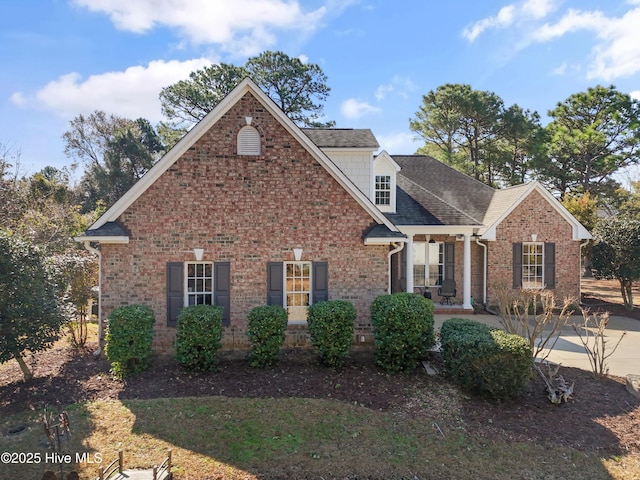 traditional-style house with a shingled roof, covered porch, and brick siding