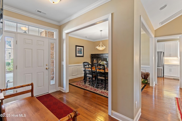 entrance foyer featuring crown molding, a wainscoted wall, visible vents, a decorative wall, and hardwood / wood-style floors