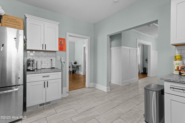 kitchen with white cabinets, light stone countertops, stainless steel fridge, and tasteful backsplash