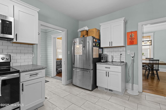 kitchen featuring white cabinets, stainless steel appliances, backsplash, and light stone countertops