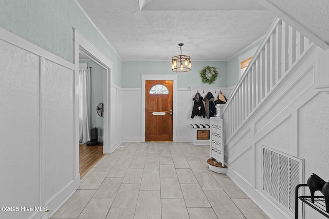 foyer entrance featuring a textured ceiling, ornamental molding, and a notable chandelier