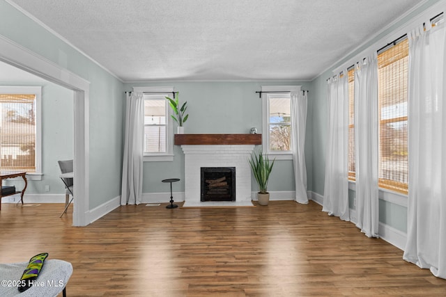 living room with a brick fireplace, hardwood / wood-style flooring, a textured ceiling, and ornamental molding