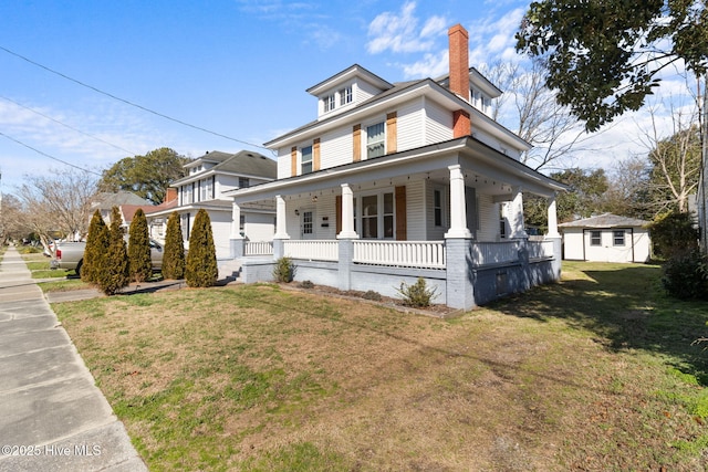 view of front facade with a porch, a front yard, and an outbuilding