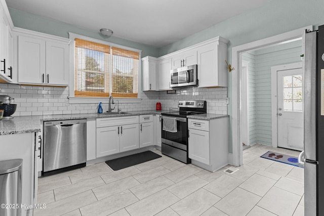 kitchen featuring appliances with stainless steel finishes, white cabinetry, light stone counters, and sink