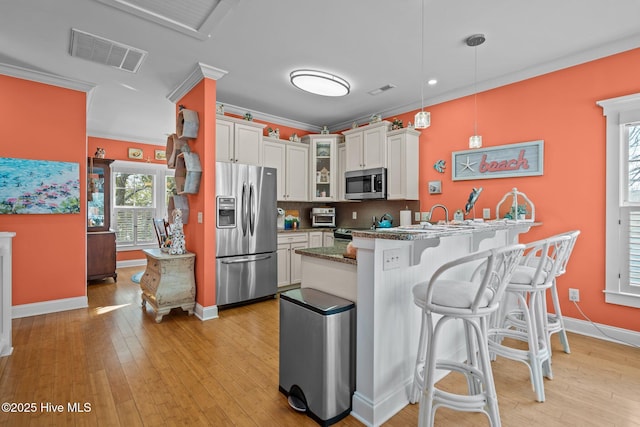 kitchen with ornamental molding, appliances with stainless steel finishes, a breakfast bar, and visible vents